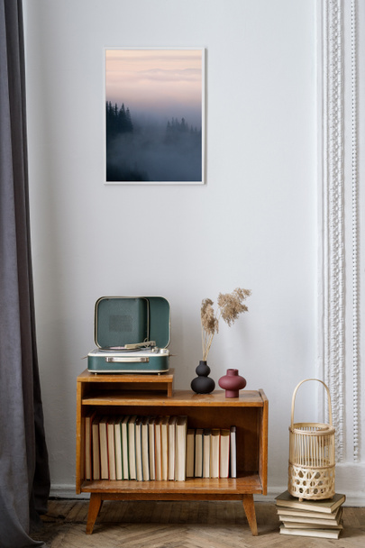Vertikale Ansicht des gemütlichen Wohnzimmers mit Vinyl-Player auf hölzernem Sideboard mit Büchern, unter Kunstbild. Dekor im Retro-Stil, Vintage-Möbel und analoge oder nostalgische Soundtechnik in der Wohnung - Foto, Bild