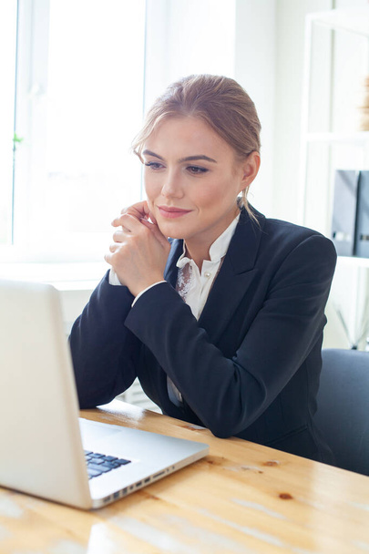 Smiling businesswoman sitting at her desk working on laptop - Zdjęcie, obraz