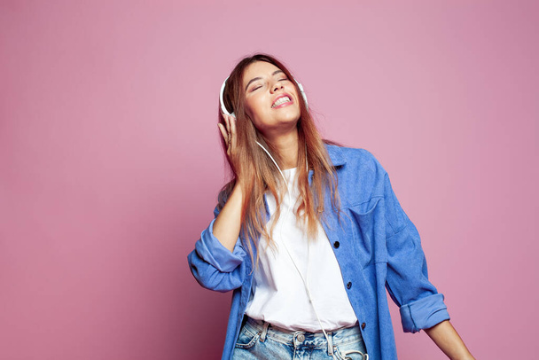 Porträt einer fröhlichen jungen Frau mit Kopfhörern, die Musik auf einem farbenfrohen rosa Hintergrund hört - Foto, Bild