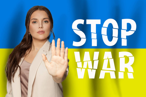 Ukrainian flag background with strong female palm hand holding stop gesture. No war in Ukraine poster - 写真・画像