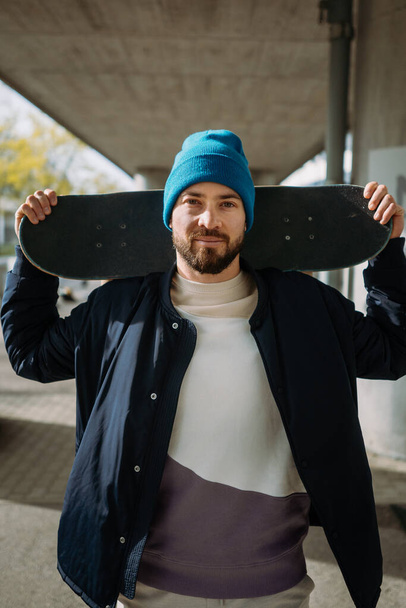 Νέοι άνδρες χαμογελαστοί Ευρωπαίοι σκέιτερ θέτουν με ένα skateboard στα χέρια. Κάθετη φωτογραφία - Φωτογραφία, εικόνα