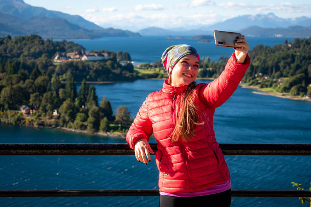 young girl taking a selfie, on a balcony overlooking a beautiful landscape, surrounded by lakes - Foto, Bild