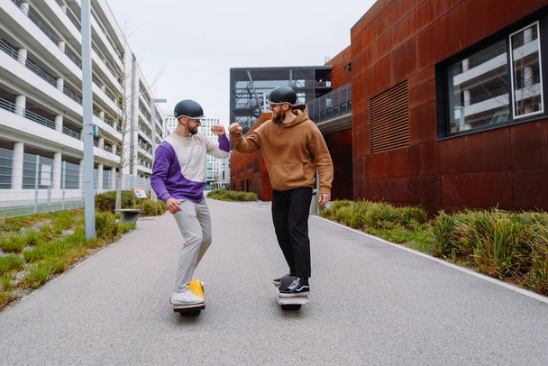 Zwei Männer auf elektronischen Skateboards salutieren mit den Ellbogen. der zukünftige Live-Stil. Urbaner Hintergrund - Foto, Bild
