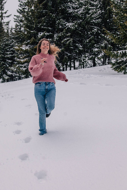 A young, slender, long-haired girl runs through the snow in a winter forest in the mountains. - Foto, Imagem