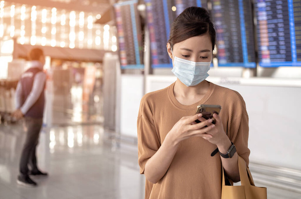 γυναίκες φοράει ιατρικές μάσκες προσώπου για να προστατευθούν από μικρόβια ρύπανσης και coronavirus και χρησιμοποιώντας συσκευή smartphone για να στείλετε ένα μήνυμα κειμένου στο αεροδρόμιο. - Φωτογραφία, εικόνα