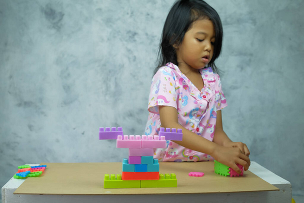 Porträt eines kleinen Mädchens, das am Tisch mit demontiertem Blockspielzeug spielt - Foto, Bild