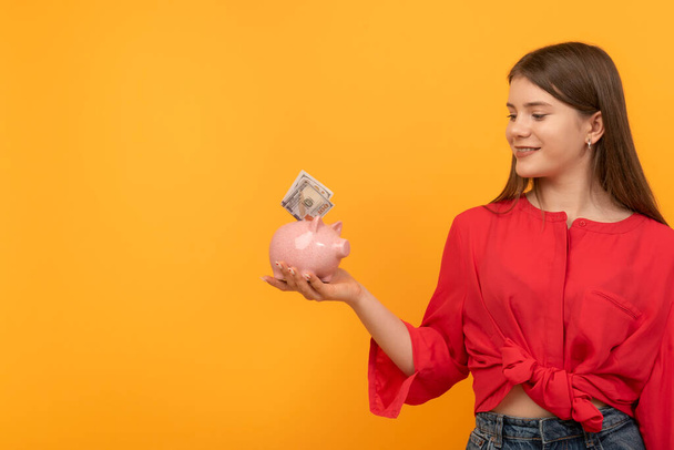笑顔の10代の少女はドルで貯金箱を持っています。お金と投資を節約する概念。財務計画、貯蓄. - 写真・画像