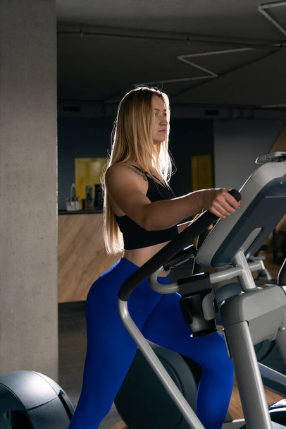 Portrait of young woman with sexy figure in the gym during workout on the orbitrek Elliptical Trainer - Фото, изображение