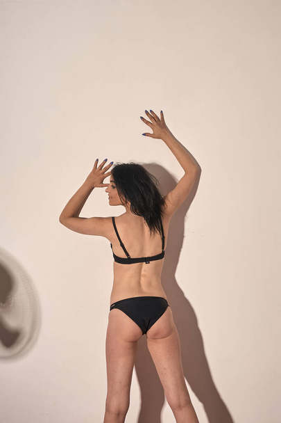 Meisje dragen bikini, poseren in studio mooie schaduw van meisje en fan op de achtergrond - Foto, afbeelding