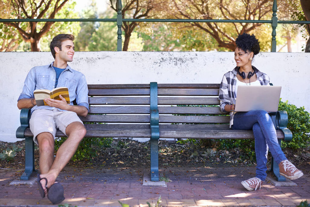 Man merkt sich zum ersten Mal. Zwei Studenten sitzen sich auf einer Bank gegenüber, ihren Lesestoff vor sich und schauen einander an.. - Foto, Bild