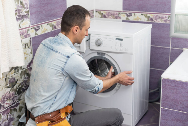 working man plumber repairs a washing machine in laundry - Foto, Bild