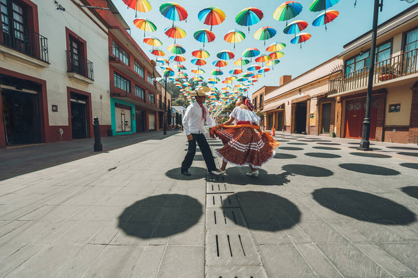 Tänzer typischer mexikanischer Tänze aus der zentralen Region Mexikos, die auf der mit bunten Regenschirmen geschmückten Straße auftreten. - Foto, Bild