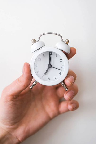 a person's hand holds a white alarm clock on a light background close-up - 写真・画像