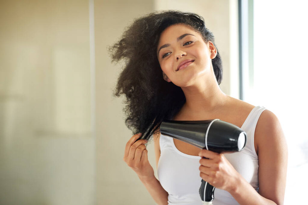 From wet to full and fabulous. Shot of an attractive young woman drying her hair with a hairdryer at home. - Foto, imagen