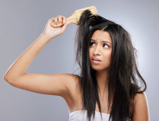 Postupujte podle osvědčených postupů péče o vlasy, aby se zabránilo poškození. Studio záběr mladé ženy s poškozenými vlasy pózovat na šedém pozadí. - Fotografie, Obrázek