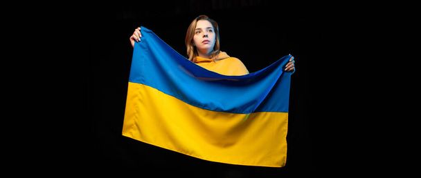 Belle fille ukrainienne avec le drapeau national de l'État de l'Ukraine sur fond noir. Espace de copie. Guerre d'Ukraine russe. Aide et priez pour l'Ukraine. Arrêtez la guerre. - Photo, image