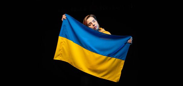 Hermosa chica ucraniana con la bandera nacional del estado de Ucrania sobre fondo negro. Copiar espacio. Guerra Ruso Ucraniana. Ayuda y reza por Ucrania. Alto a la guerra. - Foto, imagen