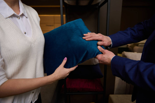 Primer plano de las manos de los clientes tocando una almohada de pie cerca de un soporte con cojines en la tienda de muebles - Foto, Imagen