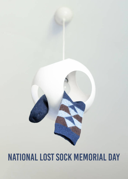 Jedna kosočtvercová kostkovaná ponožka visící ze stropního lustru. National Lost Sock Memorial Day Concept. Název dovolené je napsán nad obrázkem. - Fotografie, Obrázek