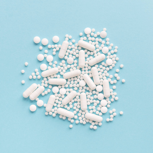 White pills on a pastel background. Capsules and round pills close-up. Healthcare and medicine. - Foto, afbeelding