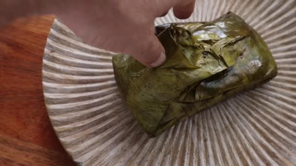 Hand unwrapping an Oaxacan Tamale made with mole wrapped in a banana leaf. - Кадры, видео