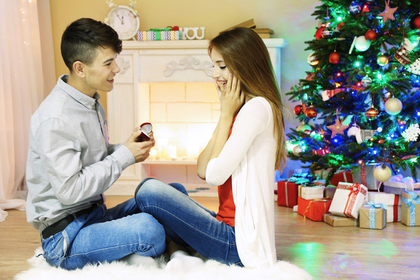Young couple sitting on carpet, at home. Man holding box with wedding ring - Foto, Imagem