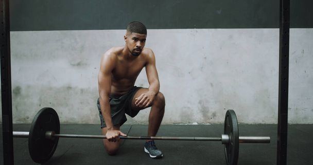 Cuando te enfrentes a un desafío, no corras hacia la salida. Retrato de un joven musculoso haciendo ejercicio con una barra en un gimnasio. - Foto, imagen