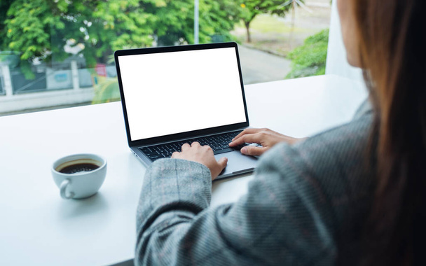 Mockup kép egy üzletasszony segítségével és gépelés laptop billentyűzet üres fehér asztali képernyő az irodában - Fotó, kép