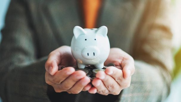 Closeup image of a woman holding piggy bank and coins in hands for saving money and financial concept - Фото, изображение