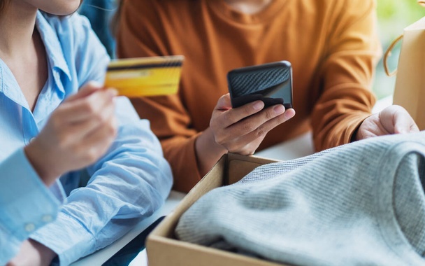 Dwie kobiety korzystające z telefonu komórkowego i karty kredytowej do zakupów online z torbą na zakupy i skrzynką pocztową na ubrania na stole - Zdjęcie, obraz