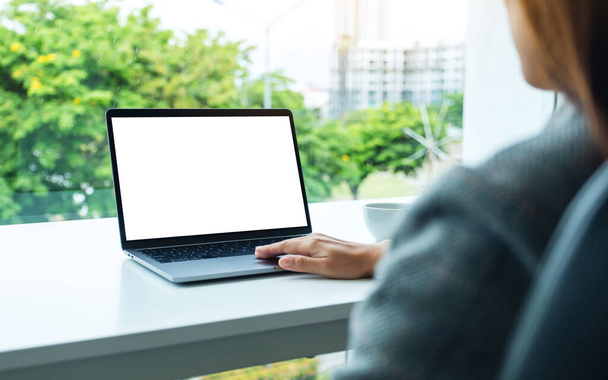 Mockup afbeelding van een hand met en aanraken op laptop touchpad met blanco witte desktop scherm in het kantoor - Foto, afbeelding