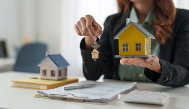 Asian real estate agent holding house key to his client after signing contract,concept for real estate, moving home or renting property - 写真・画像
