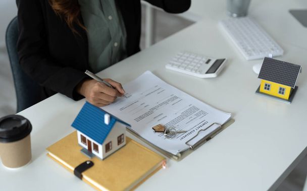 Mujer de negocios asiática firma contrato detrás del modelo de arquitectura en casa - Concepto de bienes raíces - Foto, Imagen