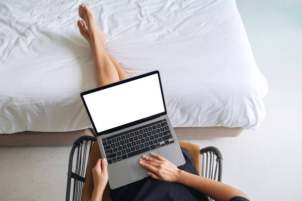 Imagen de maqueta de vista superior de una mujer trabajando y tocando el touchpad portátil con pantalla en blanco mientras está sentada en el dormitorio en casa - Foto, imagen