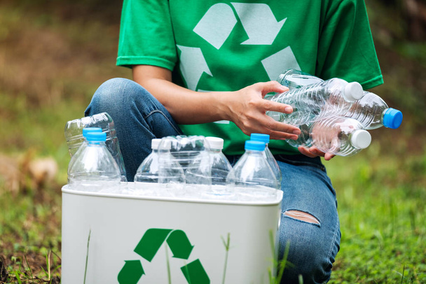 Una mujer recogiendo y poniendo botellas de plástico en una papelera de reciclaje al aire libre - Foto, Imagen