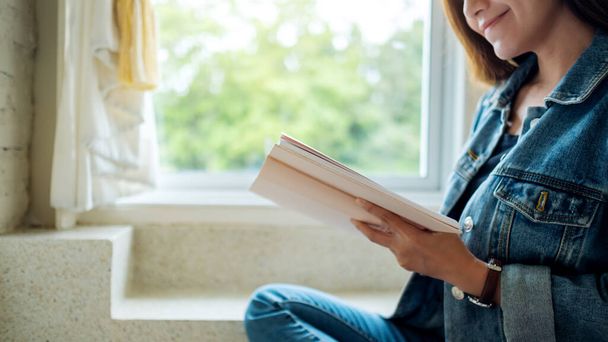 Крупним планом зображення красивої азіатки сидить і читає книгу вдома
 - Фото, зображення