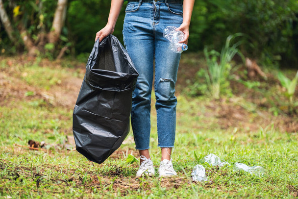 Szoros kép egy női aktivistáról, amint szemetes műanyag palackokat szed fel egy műanyag zacskóba a parkban újrahasznosítás céljából. - Fotó, kép