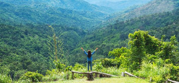Rear view image of female traveler raising arms while looking at a beautiful green mountains view - Foto, Imagen