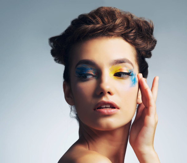 Von der Kunst inspiriertes Make-up. Studioaufnahme einer attraktiven jungen Frau mit buntem Make-up vor grauem Hintergrund. - Foto, Bild