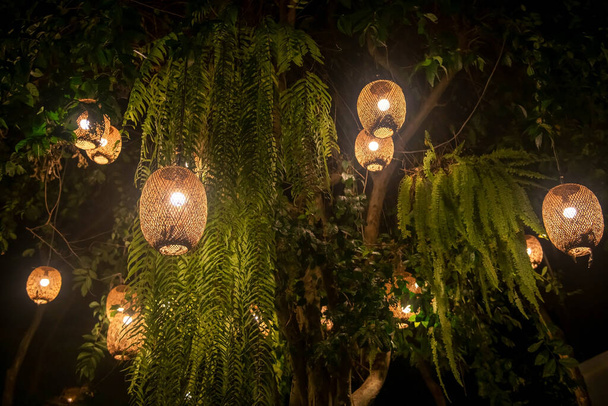 Dekoráció lógó lámpás villanykörték a fán éjjel a szabadtéri parkban. Fa bambuszból készült lámpák. - Fotó, kép