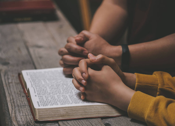 Zbliżenie dwóch chrześcijan czytających Biblię. Ręce złożone w modlitwie na Biblii na drewnianym stole. kult grupowy online, Światowy Dzień Modlitwy, Międzynarodowy Dzień Modlitwy, Nadzieja, Wdzięczność, Wdzięczność, zaufanie - Zdjęcie, obraz