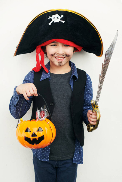 Playful pirate. Shot of a little boy dressed in a pirate costume while holding a jack o lantern against a white background. - Foto, Imagem