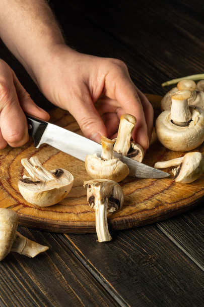 Affettare funghi Agaricus su un tagliere dalle mani di uno chef con un coltello per preparare un delizioso piatto nazionale. - Foto, immagini