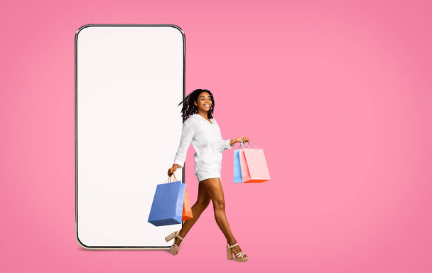 Зачарована гаряча чорна молода жінка з покупками та мобільним телефоном
 - Фото, зображення