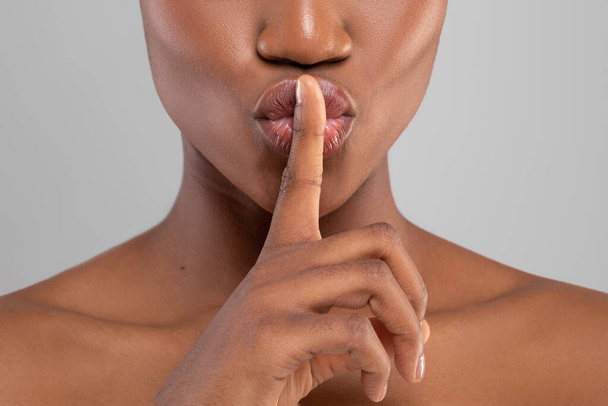 Веселая красивая молодая черная женщина с идеальной кожей делает знак молчания, изолированные на сером фоне, обрезанный - Фото, изображение