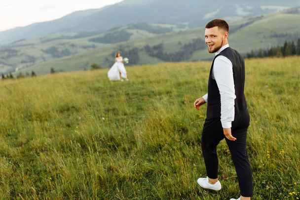 schönes junges verliebtes Hochzeitspaar posiert vor dem Hintergrund der Berge - Foto, Bild