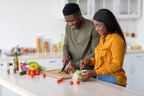 Romantisches schwarzes Paar kocht gemeinsam in der Küche und bereitet zu Hause gesunde Lebensmittel zu - Foto, Bild