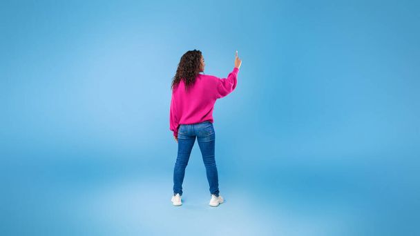 Back view of millennial African American lady touching imaginary screen, pressing button, using virtual interface - 写真・画像