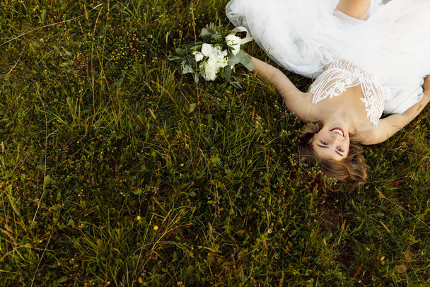 beautiful young bride in white dress lying on grass   - Photo, Image