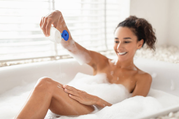 Mulher milenar adorável usando sabão ou espuma enquanto deitado em banho de espuma em casa, foco seletivo. Espaço livre - Foto, Imagem